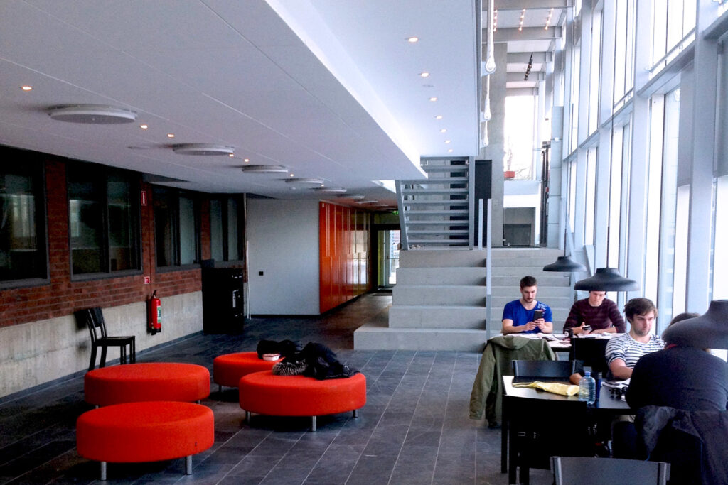 Studieyta i Matteannexet med takspotlights, orange sittpuffar och studenter vid fönsterborden.