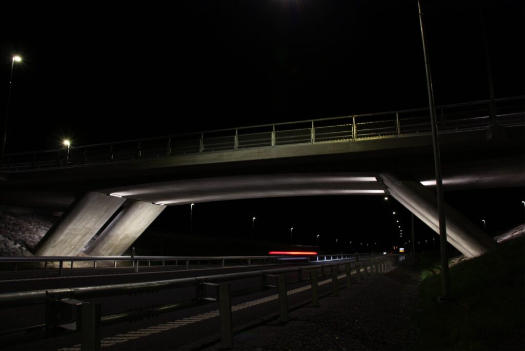 Betongöverfart vid Västra länken nattetid, undersidan och pelarna belysta i vitt.