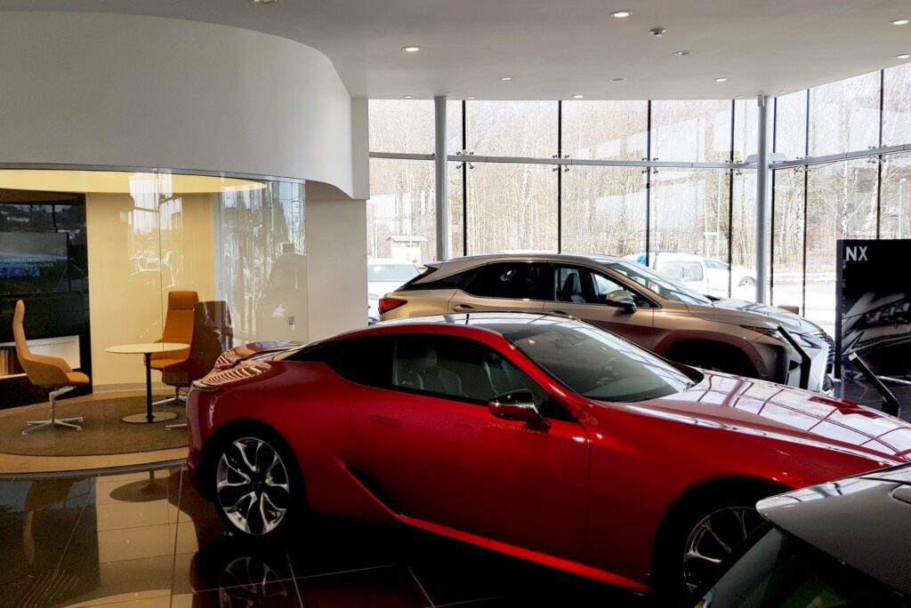 Lexus-showroom med röd sportbil, silverfärgad SUV och infällda takspots mot glasfasad.