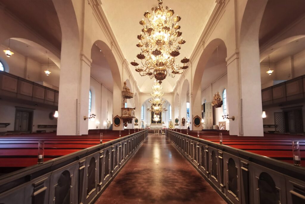 S:t Olai kyrka längs mittgången med mässingskronor, röda bänkkuddar och vitt kyrkorum.