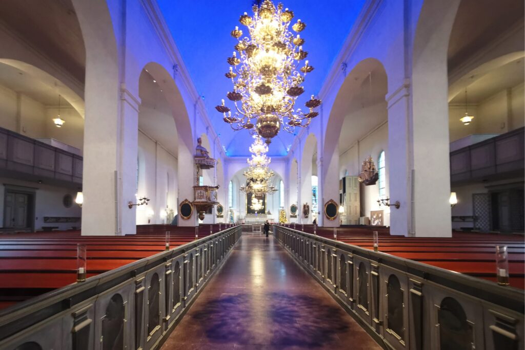 S:t Olai kyrka med himmelsblått tunnvalv, tre mässingskronor och vit pelargång mot koret.