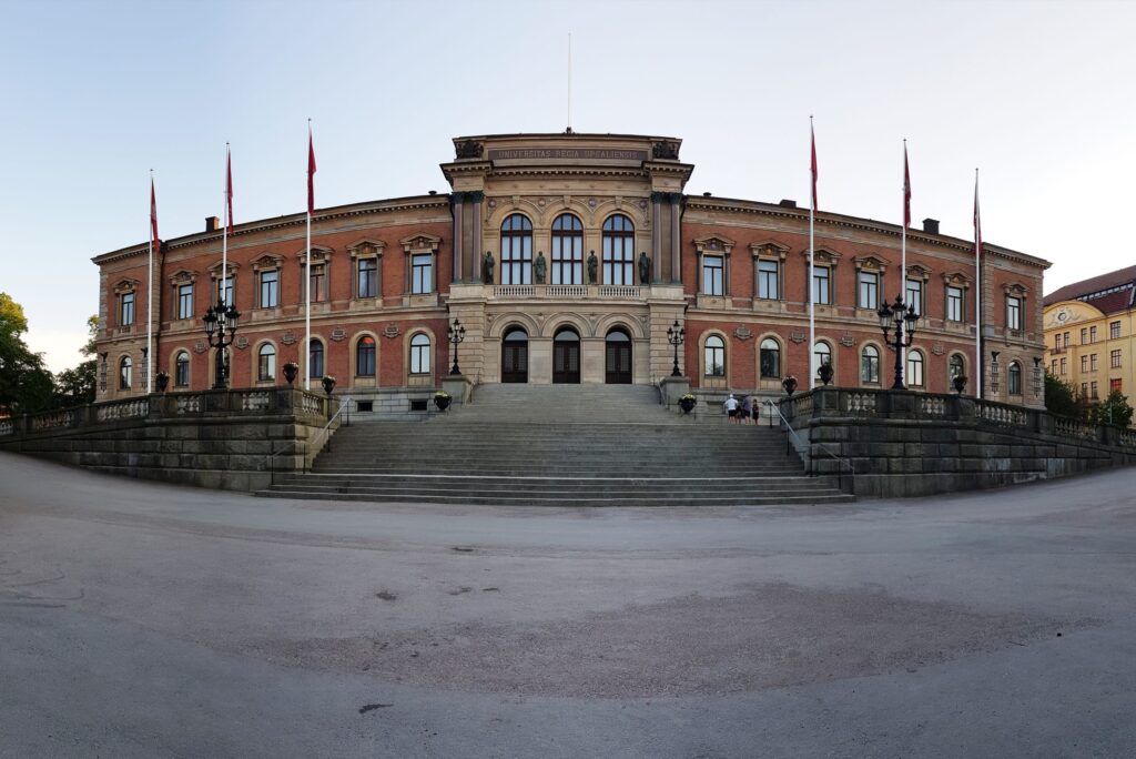 Universitetshusets tegelfasad i Uppsala med stenentré, lampstolpar och flaggstänger.