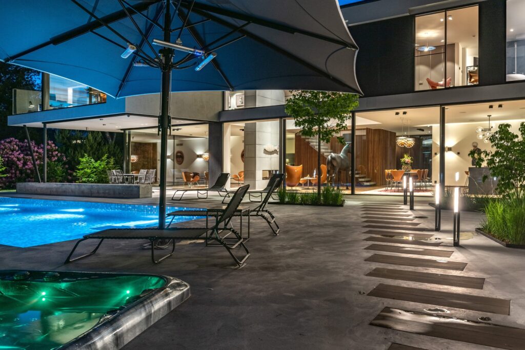 Villa i Malmö i skymning med belyst pool, pollare på uteplatsen och varmt ljus genom glasfasaden.