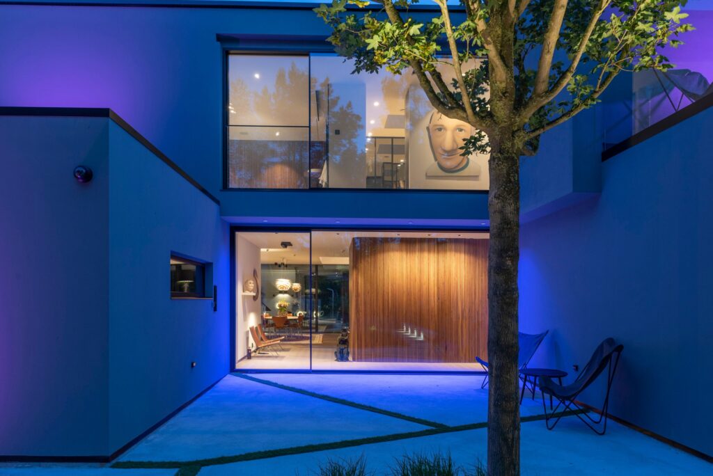 Villa i Malmö med blåviolett utebelysning på patio och varmt innomhusljus genom stora fönster.