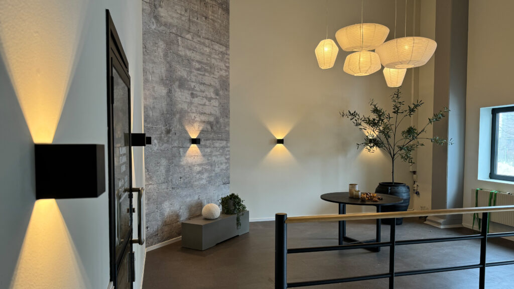 Lounge med svarta kubformade vägglampor som kastar triangulära ljuskäglor och vita pappersliknande pendlar.