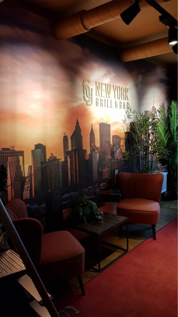 Lounge på New York Bar & Grill med skylinevägg, rostfärgade fåtöljer och takspots.