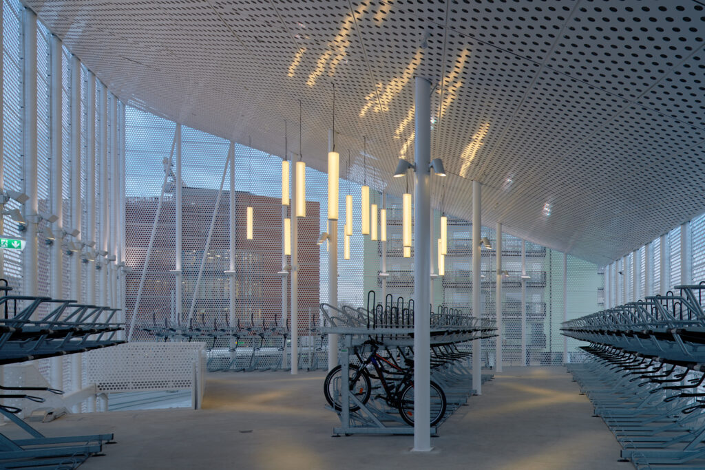 Cykelgarage med perforerat vitt tak, vertikala pendelrör och tvåvånings cykelställ.
