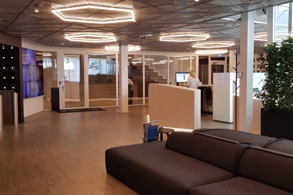 DICE-lobby med soffa, träreception, stor skärm till vänster och sexkantiga takarmaturer.