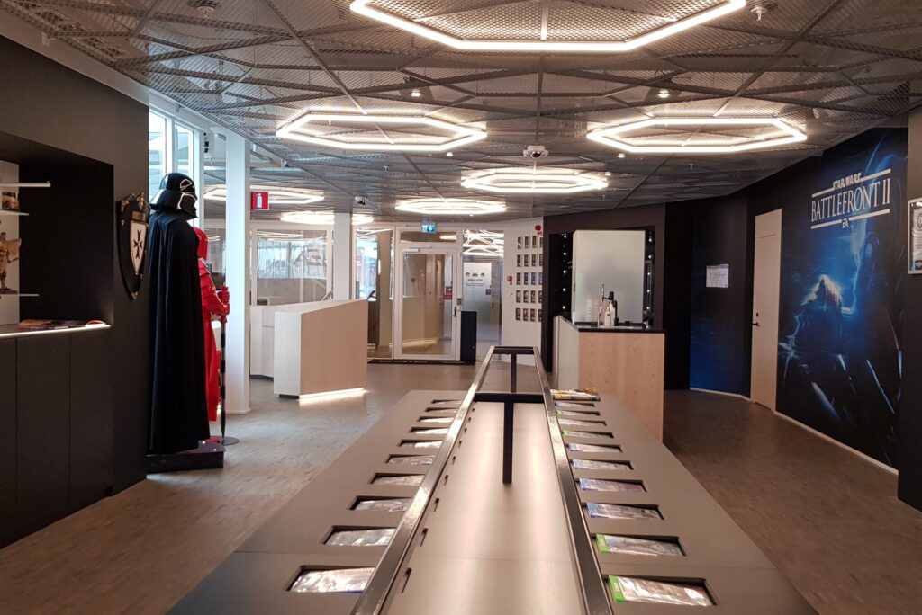 DICE-lobby med Star Wars-statyer, utställningsbord och infällda hexagonala LED-armaturer i taket.