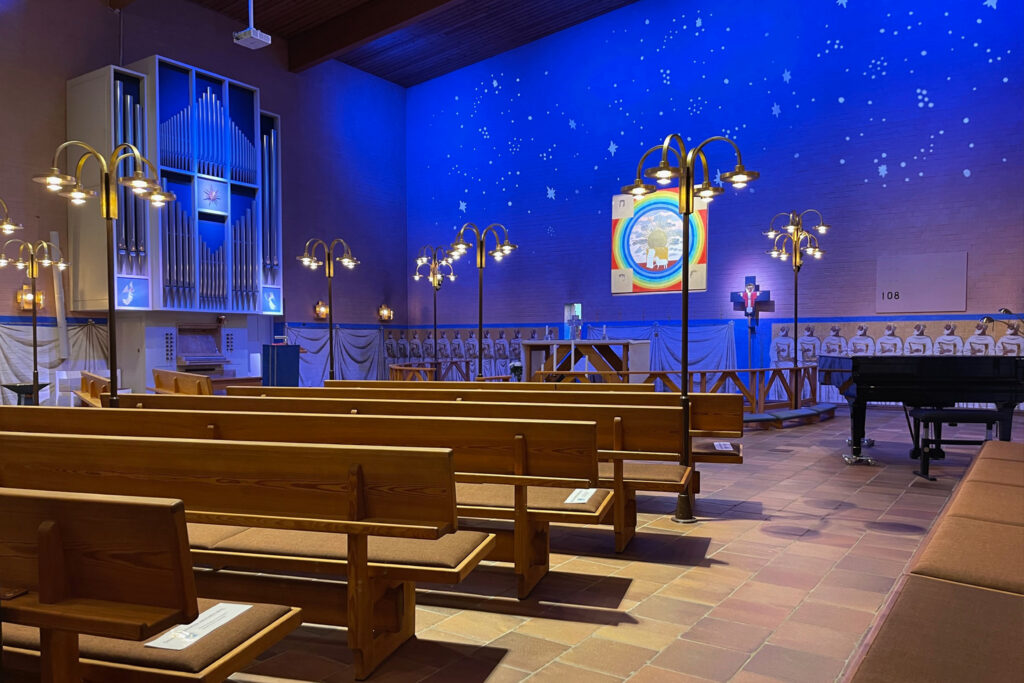 S:t Hans kyrka i Lund med blå belyst korvägg, stjärnljus och mässingsgolvlampor längs mittgången.