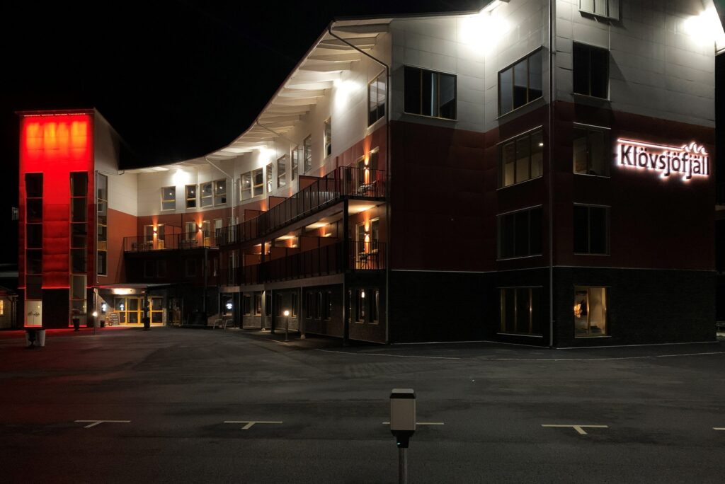 Klövsjöfjäll hotell nattetid med röd belyst tornsektion och lysande namnskylt.