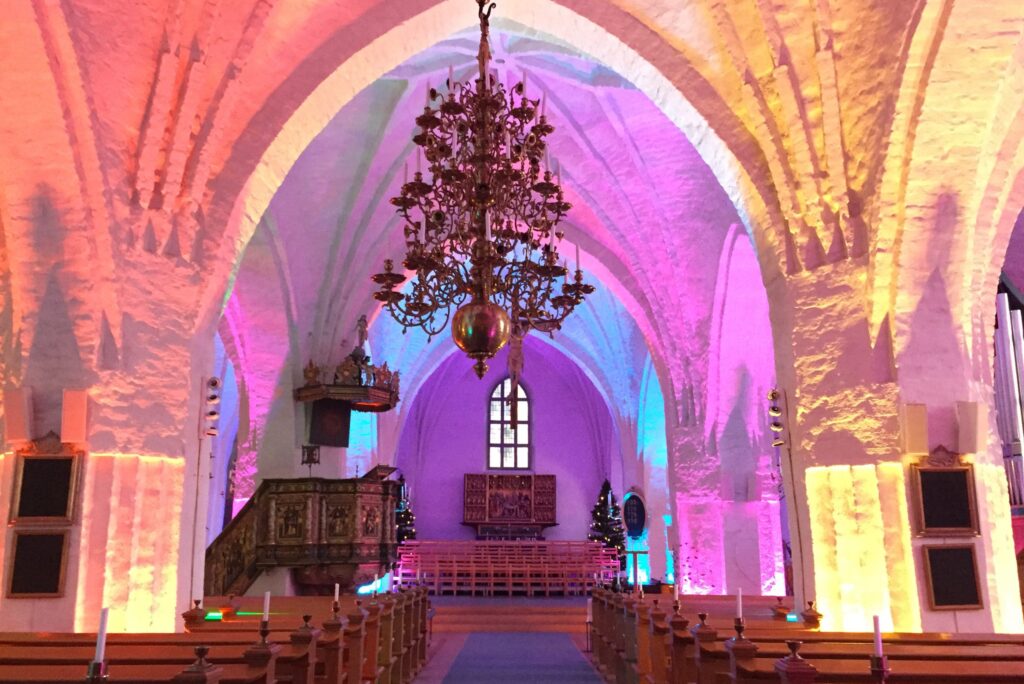 S:t Laurentii kyrka med magenta belysta stenvalv, mässingskrona och blåviolett belyst kor.