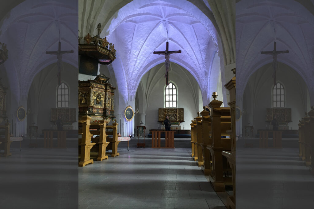 S:t Laurentii kyrka med violett belyst ribbvalv, hängande krucifix och snidad predikstol till vänster.