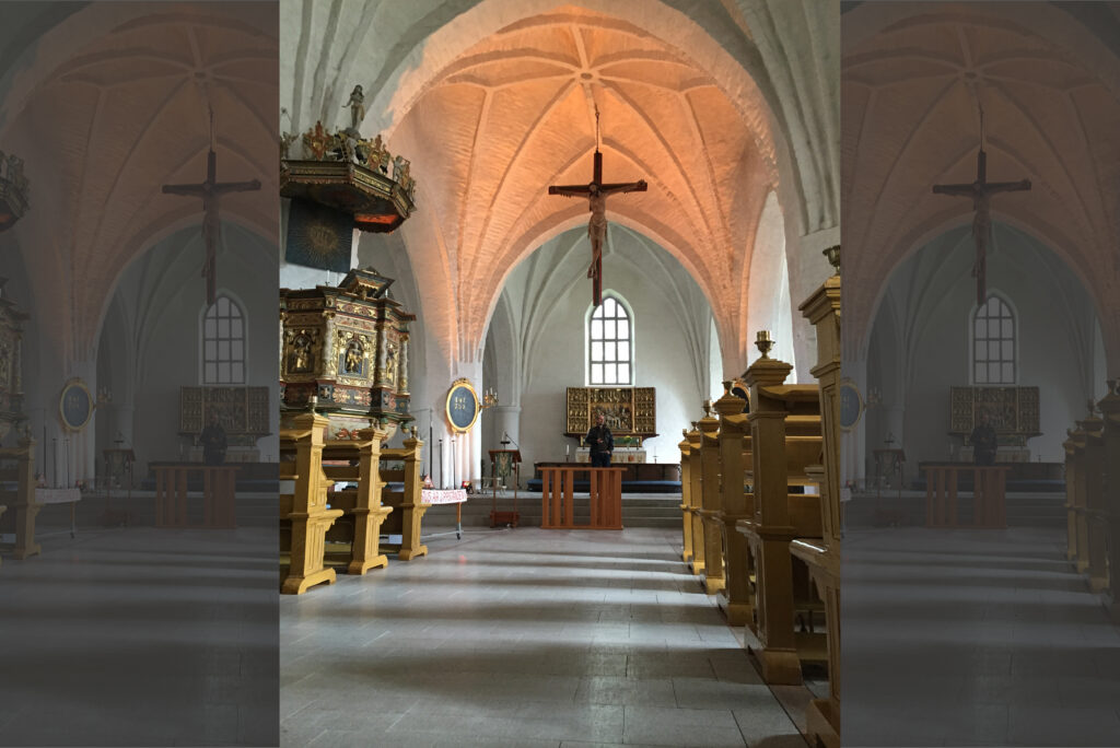 S:t Laurentii kyrka i dagsljus mot koret, med vita valv, predikstol och krucifix mot fönstret.