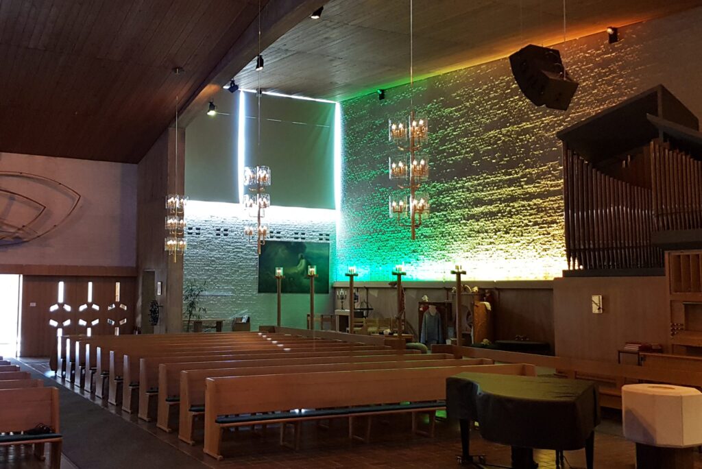 Mikaelikyrkan med lysande kors i bakväggen, grönorange belyst stenvägg och orgel till höger.