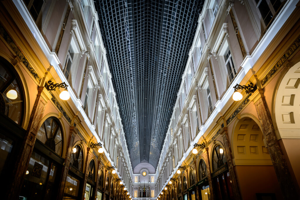 Övertäckt galleria nattetid med glas- och metallvalv och varma klotlampor längs fasaderna.