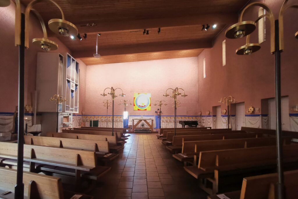 S:t Hans kyrka med terracottafärgat kyrkorum, orgel till vänster och grenade mässingslampor längs mittgången.