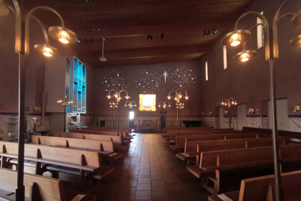 S:t Hans kyrka i dämpat ljus med stjärnhimmel på korväggen och varma golvlampor längs mittgången.