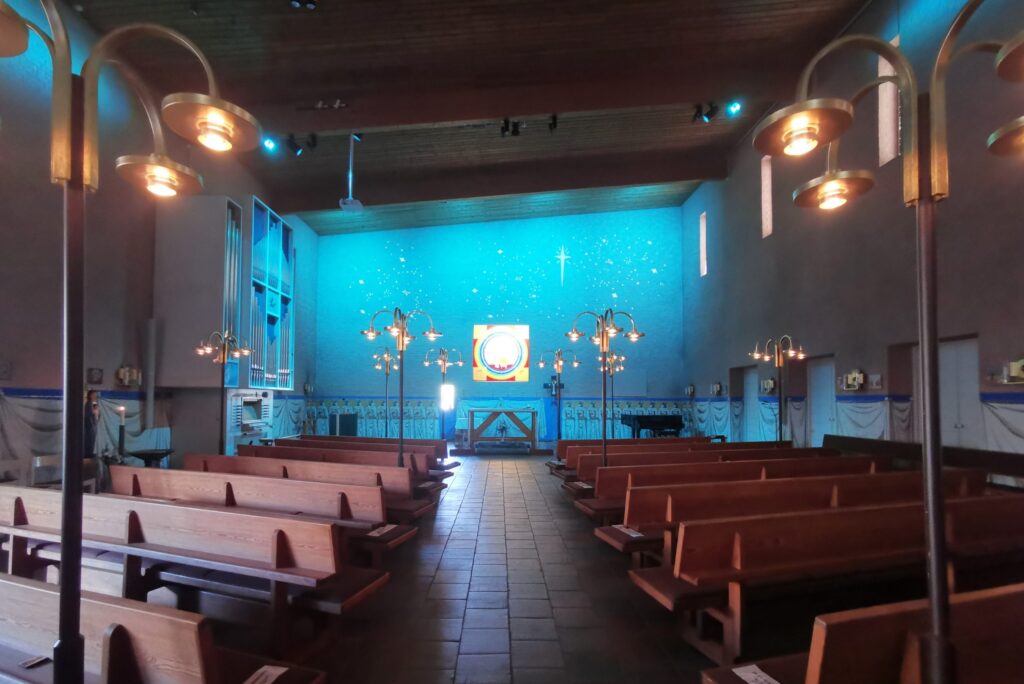 S:t Hans kyrka med cyanblå korvägg, stjärnprickar och varma cirkelformade lampor längs bänkraderna.