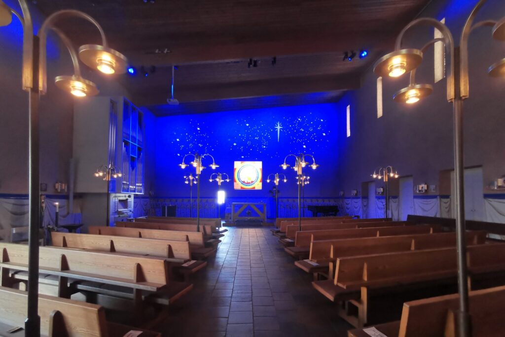S:t Hans kyrka med djupblå korvägg, lysande korsmotiv och stjärnljus ovanför ett enkelt träaltare.